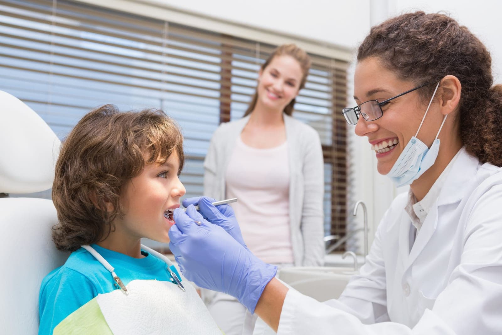 A gentle dentist examining a young child's teeth while a parent watches